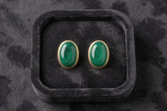 Paire de boucles d'oreilles Potala style Dragon Ball avec pierre ovale verte et monture dorée sur plateau velours noir, vue de dessus