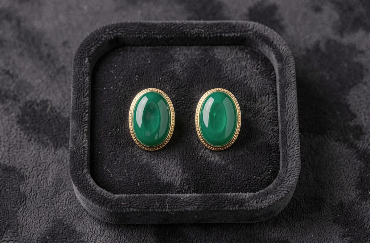 Paire de boucles d'oreilles Potala style Dragon Ball avec pierre ovale verte et monture dorée sur plateau velours noir, vue de dessus